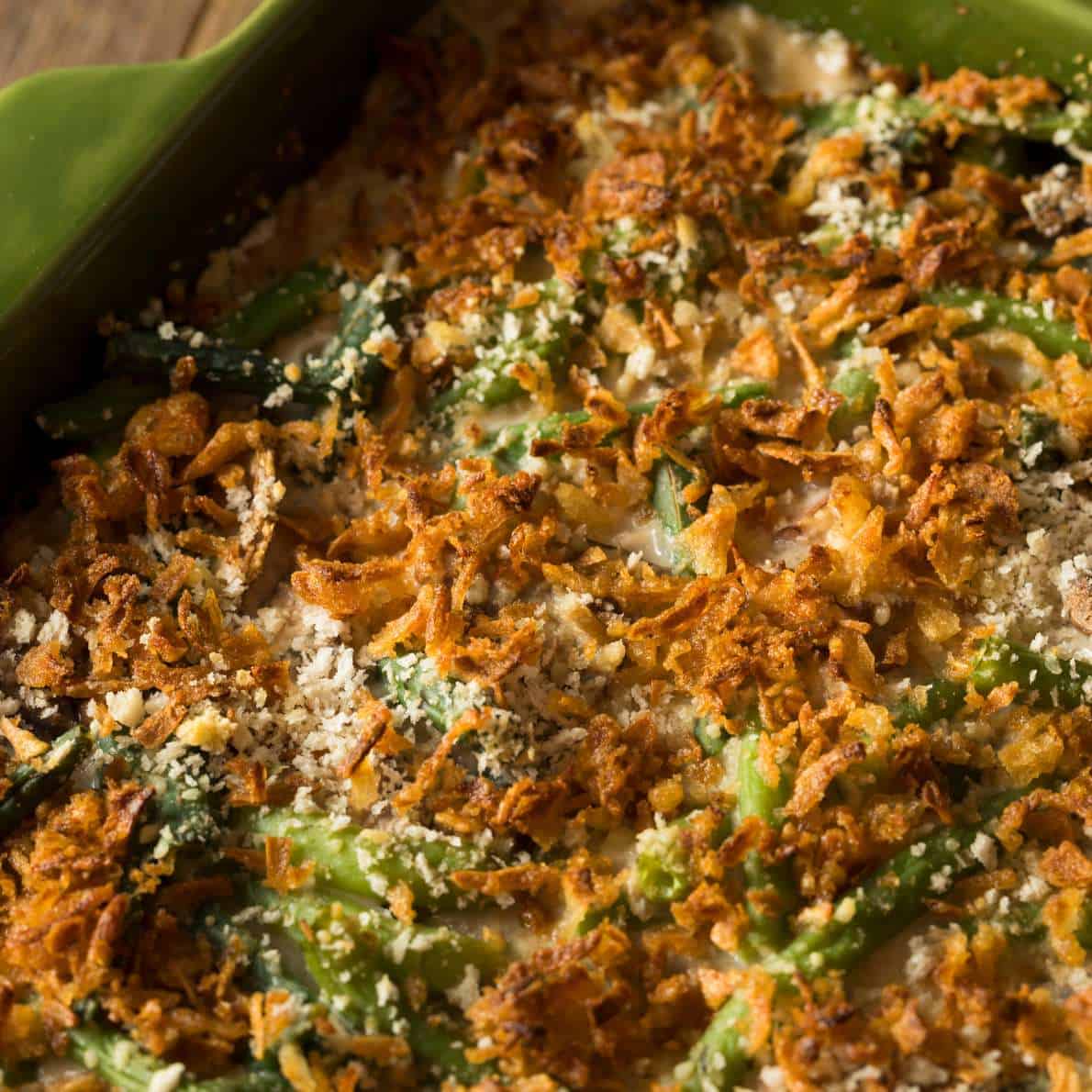 Close-up of a green bean casserole, perfect for using leftovers from Thanksgiving, topped with crispy fried onions and breadcrumbs in a green baking dish. The golden brown topping looks irresistibly crunchy.