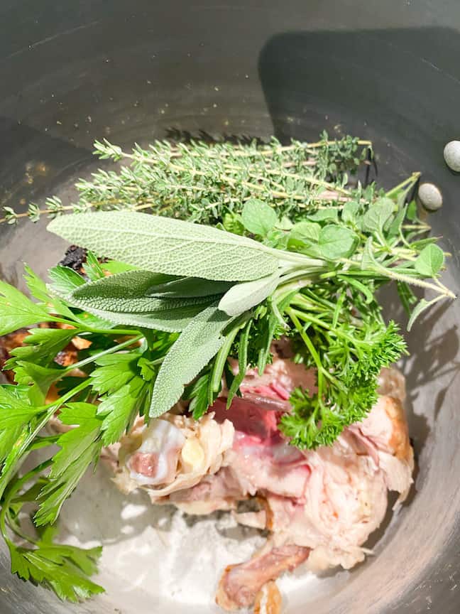 pot with chicken bones and fresh herbs to make chicken stock for chicken noodle soup