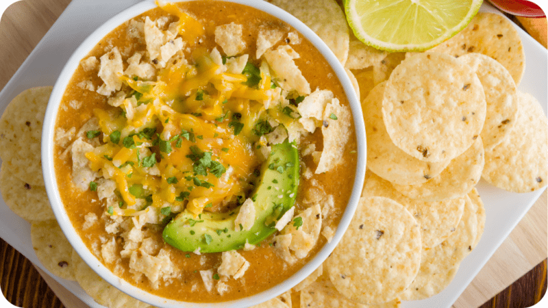 chicken noodle soup with cheddar cheese, tortillas and avocado on top