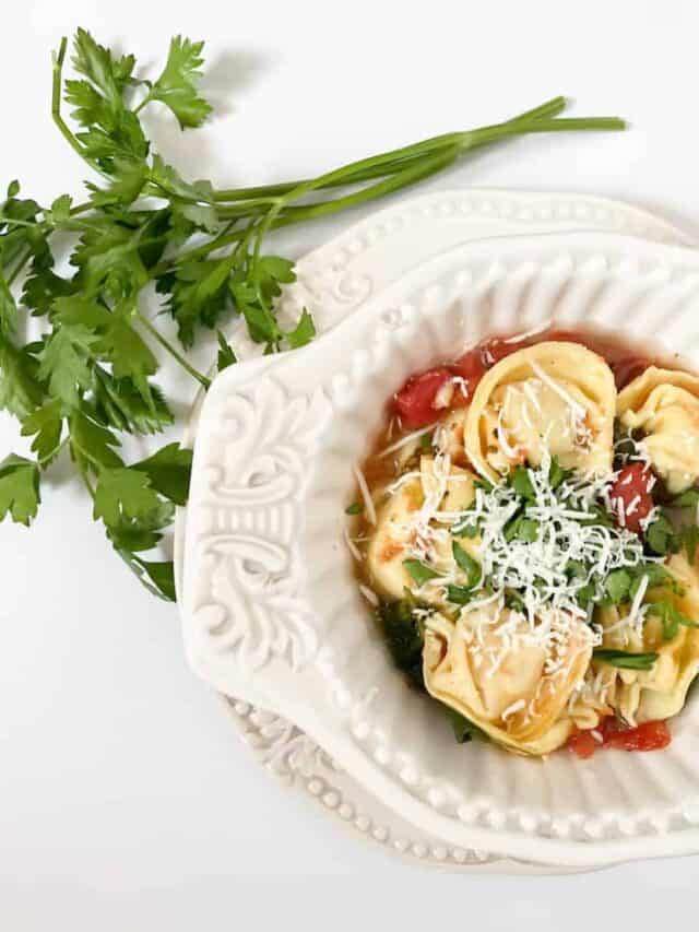 a bowl of tortellini spinach soup with a piece of parsley next to it