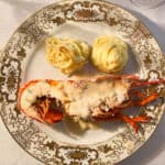 a plate with a cook whole lobster with duchess potatoes on a white and gold china plate