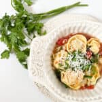 a bowl of tortellini spinach soup with a piece of parsley next to it