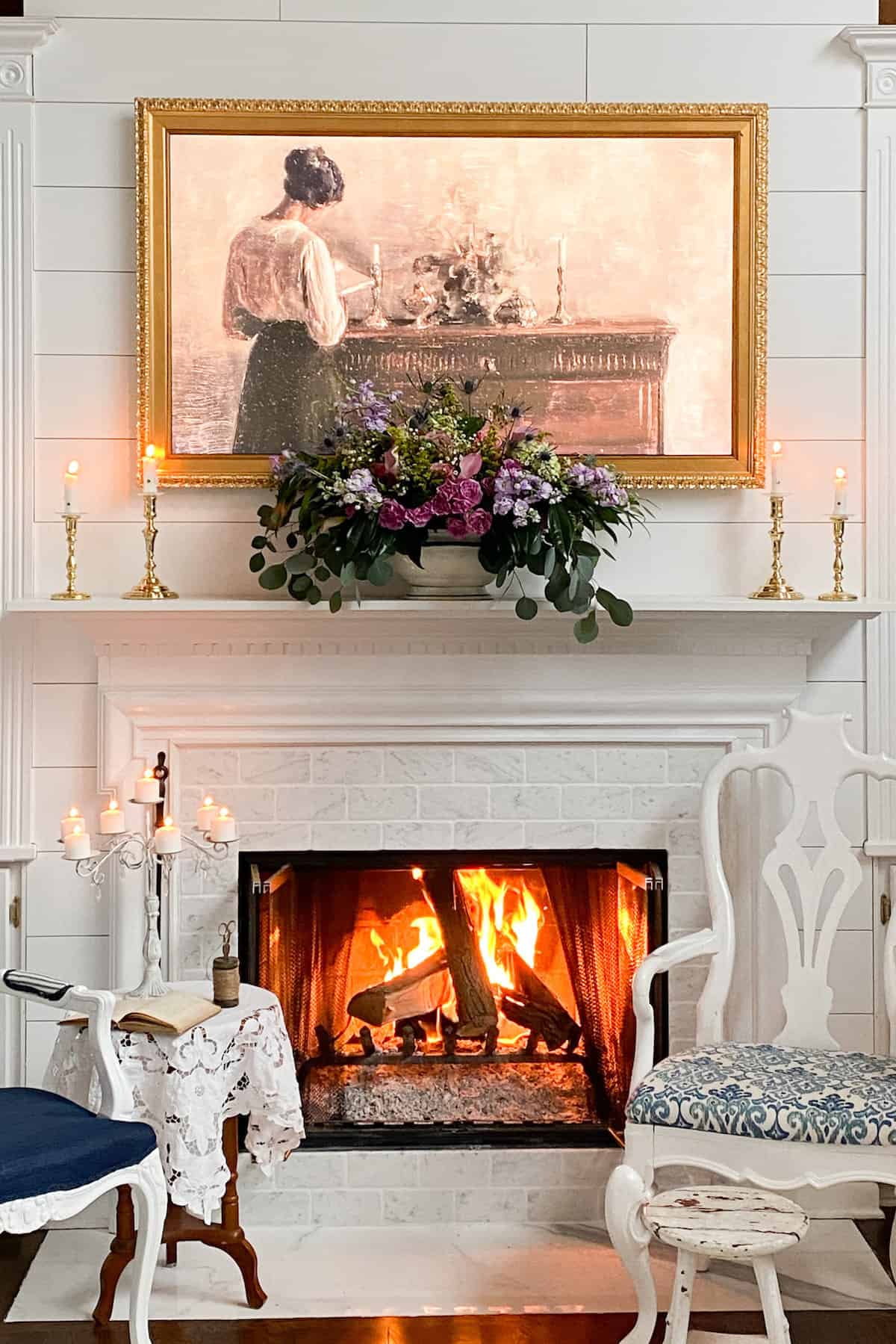 beautiful fireplace picture. fire is lit. there is a large floral arrangement on the mantel flanked by candles. the frame tv with a vintage photo on it.