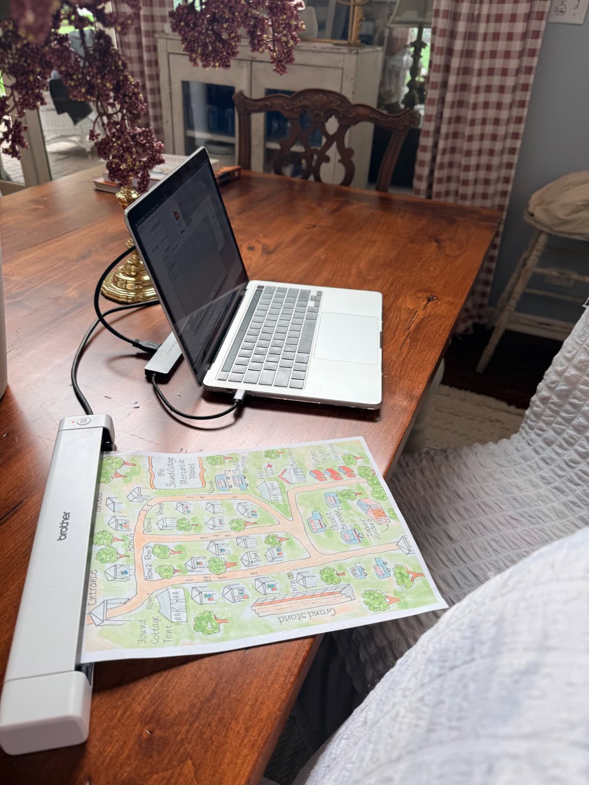 A laptop and scanner on a wooden table help with organizing my paperwork by digitizing a colorful hand-drawn map.