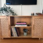 Wooden cabinet with patterned doors, books, plants, a candle, records, and a remote adds vintage 1960s home decor flair.