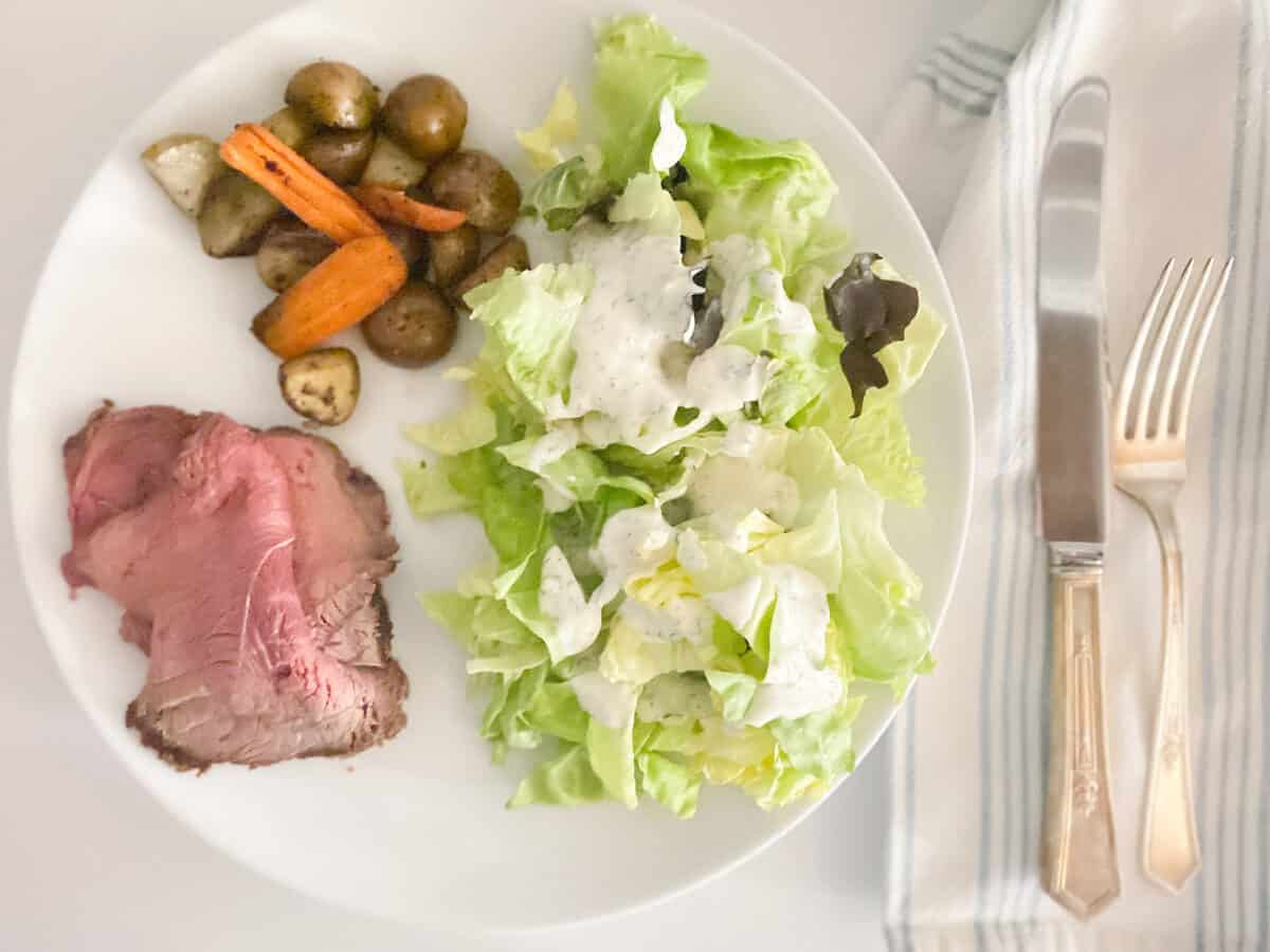 plate with sliced beef roast, roasted vegetables and a side salad