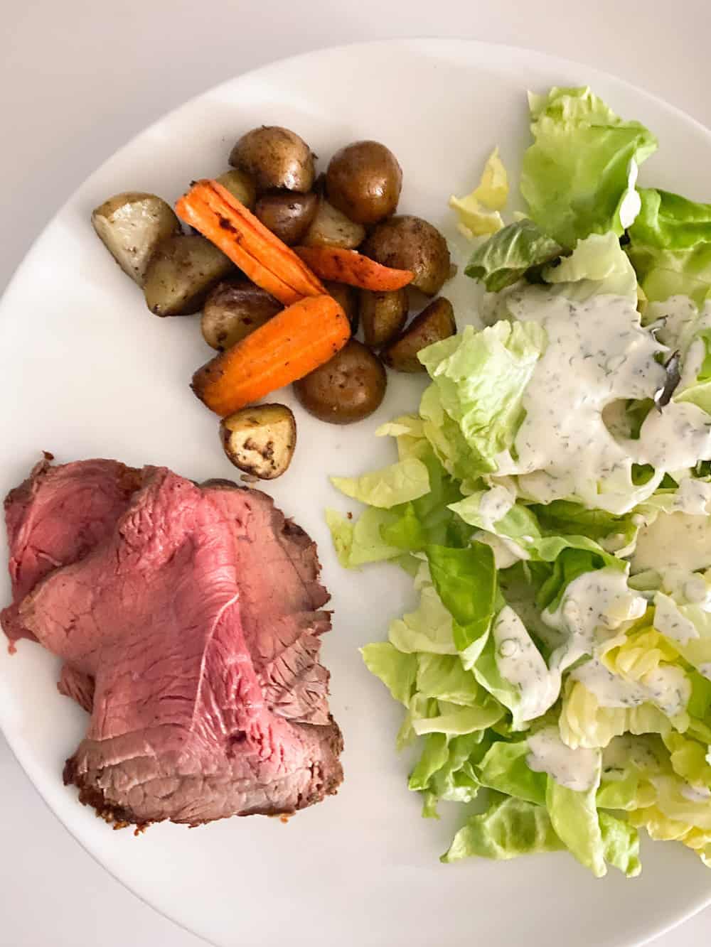 plate with sliced beef roast, roasted vegetables and a side salad