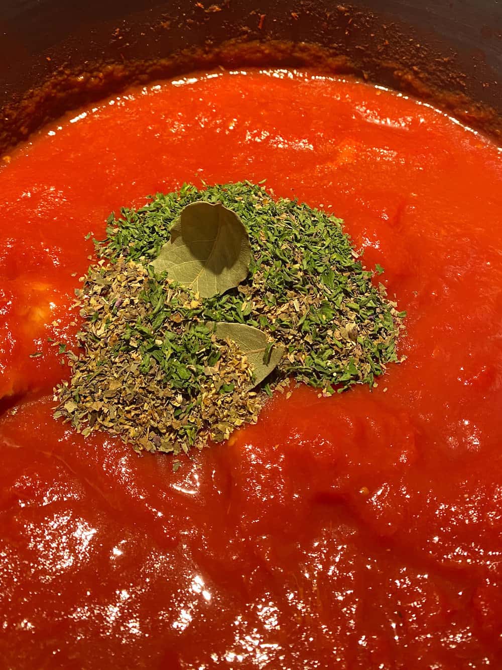 photo of the spices on top of the tomato puree in a stock pot. The making of traditional Italian pasta sauce