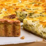 A close-up of a golden-brown quiche with a thick, flaky crust, filled with creamy cheese and vegetables. A wedge is cut and slightly pulled out—perfect for easter sunday brunch menu ideas, showcasing its rich, layered interior.