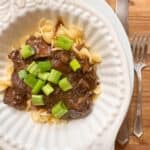 Beef sirloin tips and onion gravy in a bowl garnished with green onions