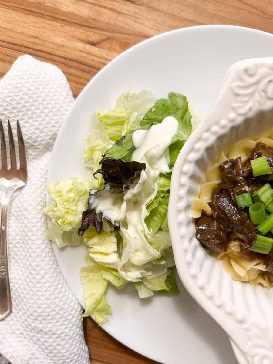 Beef sirloin tips and onion gravy in a bowl garnished with green onions and served with a side salad