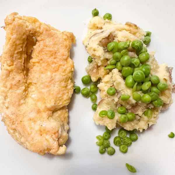 chicken with smashed potatoes and horseradish garnished with peas.