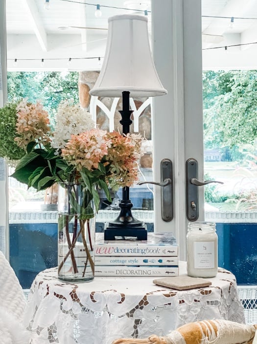 a vintage end table with flowers, a lamp, books and a candle on it.