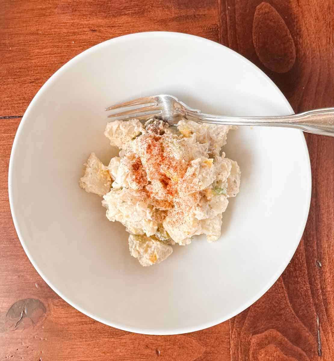 potato, chicken, dill pickle salad in a white bowl with a fork