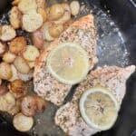 cooked potatoes in cast iron pan with chicken breast browned on one side and flipped with lemon slices on the top