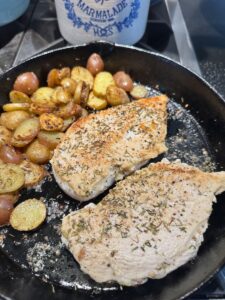 cooked potatoes in cast iron pan with chicken breast browned on one side and flipped
