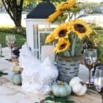 tablescape for an outdoor dinner party with pumpkins, sunflowers, and large wooden candle holder