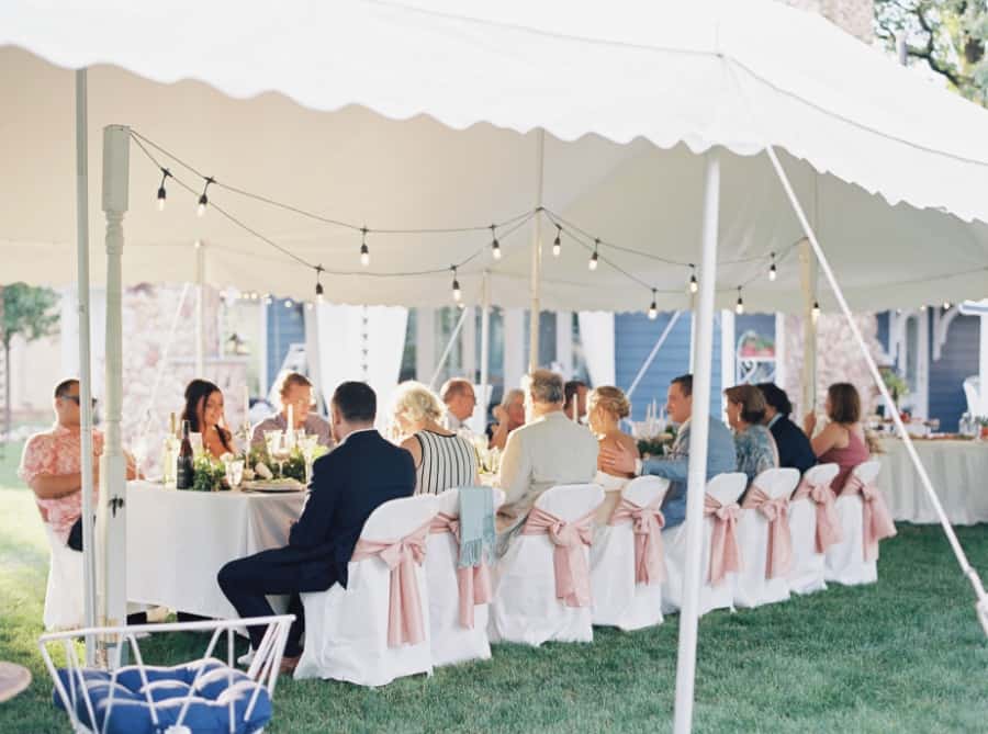 All the guests seated for dinner under the tent at the backyard wedding.