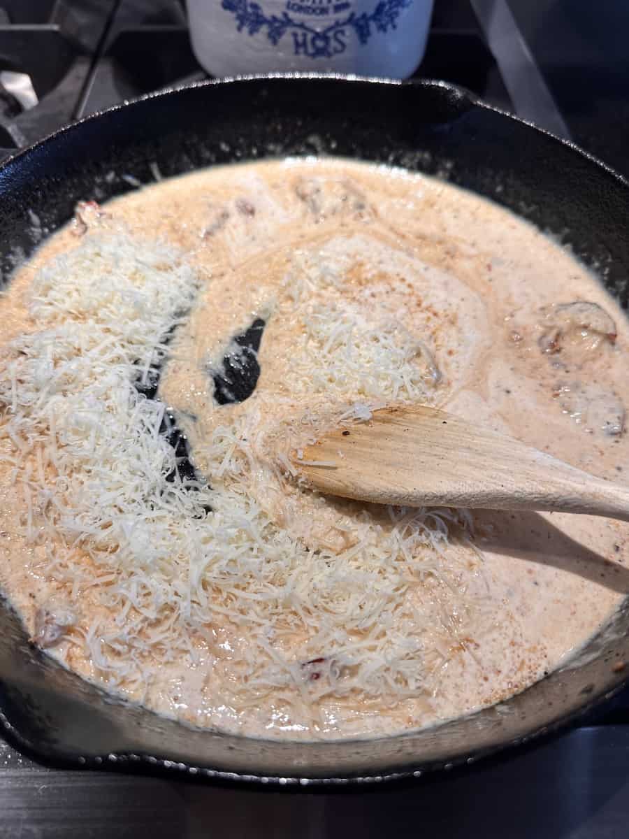adding cheese to sun-dried tomato cream sauce