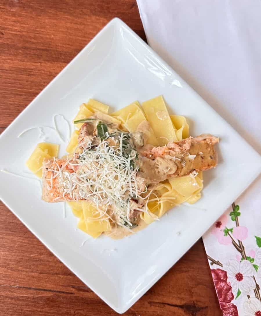 sun-dried tomato cream sauce served over pappardelle pasta and salmon on a white square plate