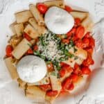 a bowl of pasta with burst cherry tomatoes topped with burrata cheese