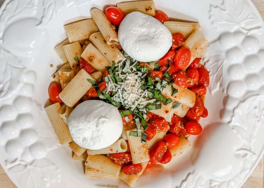 a bowl of pasta with burst cherry tomatoes topped with burrata cheese