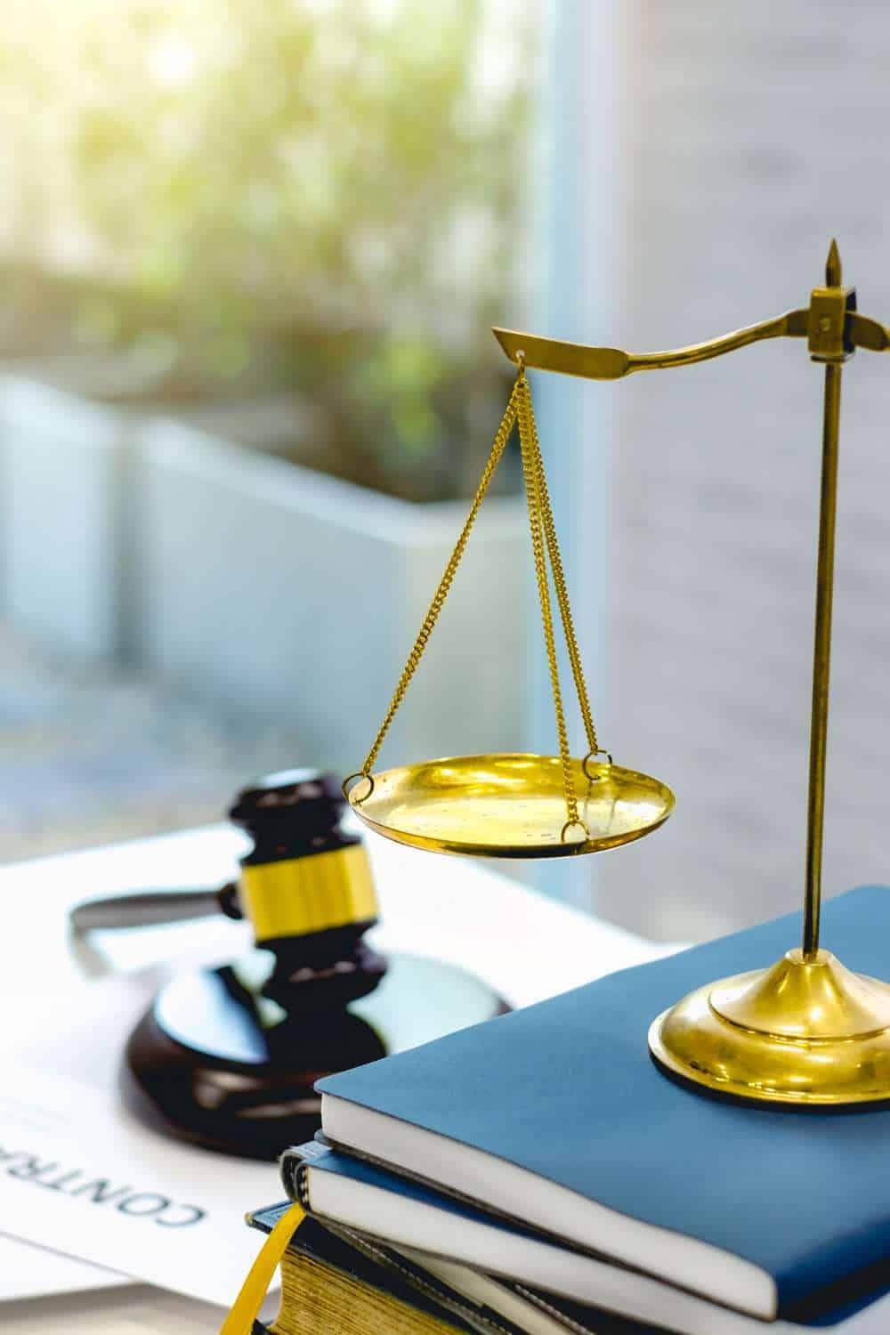 A brass balance scale sits on blue books next to a wooden gavel, symbolizing law and justice, with a contract partially visible in the background—invoking recollection of landmark legal moments.