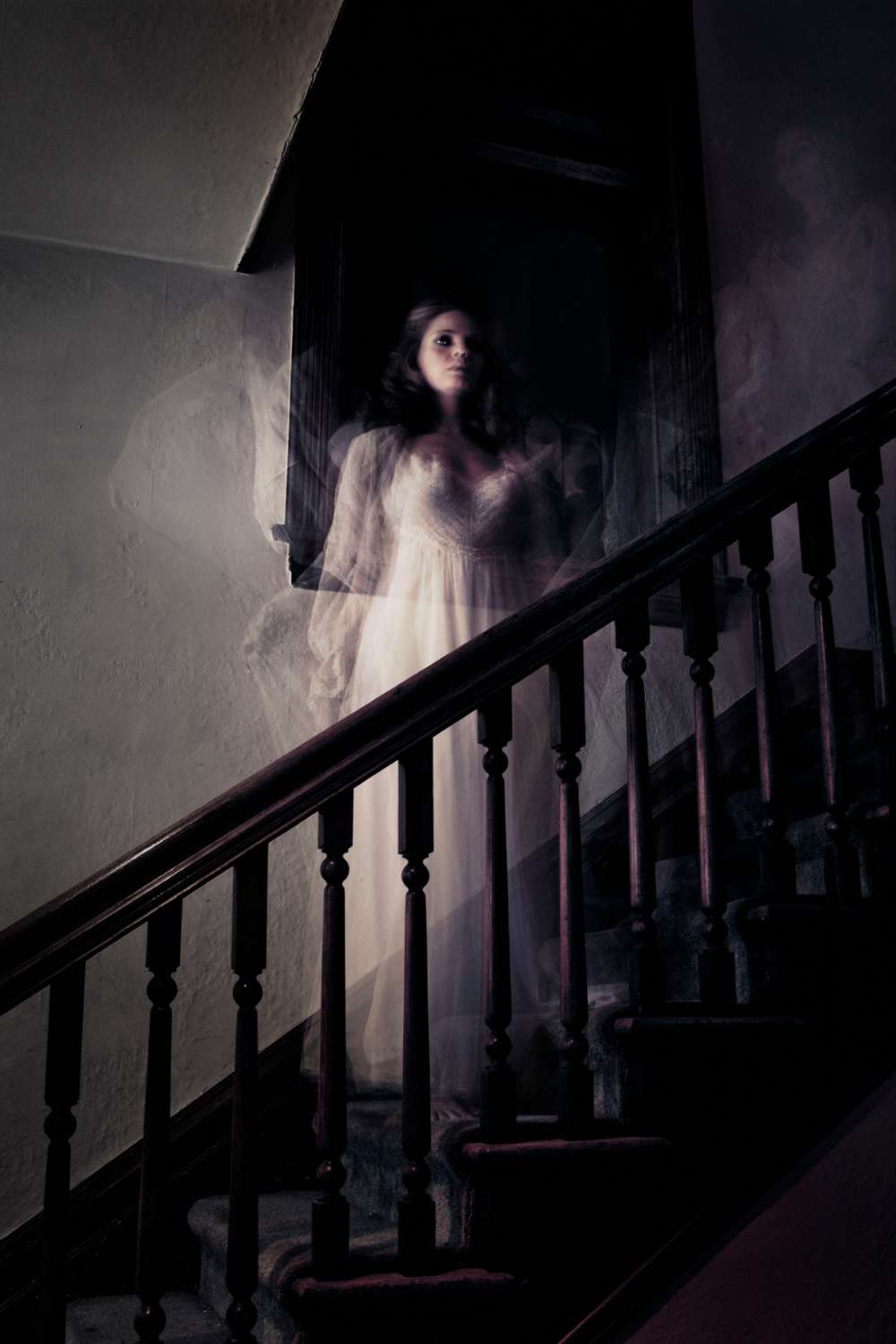 A ghostly woman in a white dress stands on a dimly lit staircase, her figure blurred and semi-transparent, as if a fleeting recollection haunting the dark hallway with an ethereal atmosphere.