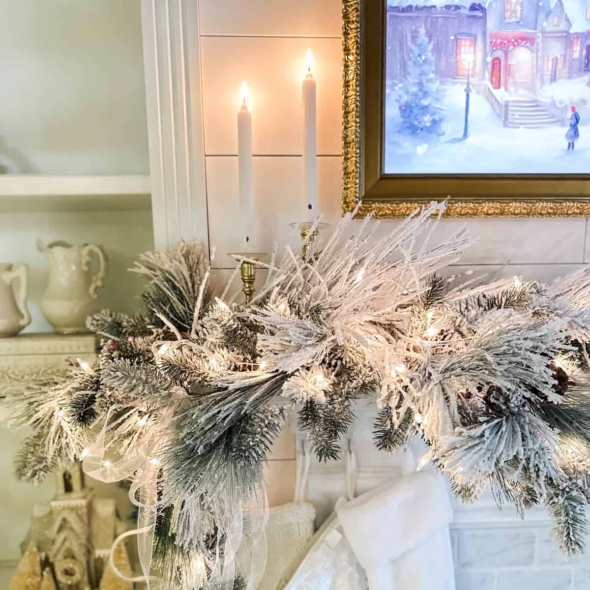 corner of the living room fireplace mantel showing the details of the frame tv, brass candle sticks and faux flocked greenery