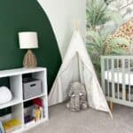 a corner of the room with a view of the bookshelve wall, toy tent, and mural wall with a crib