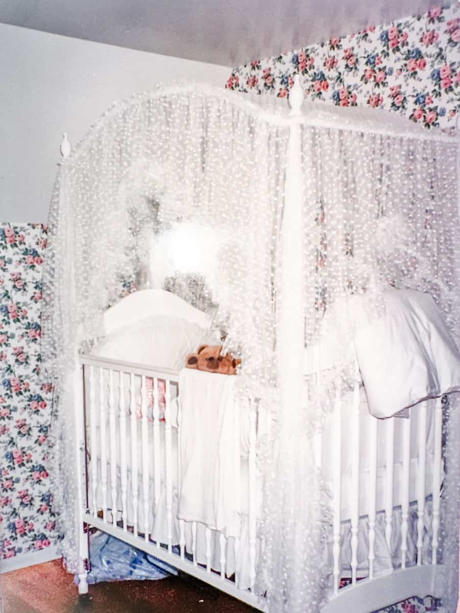 Annie's baby nursery with pink and white floral wallpaper and a white crib draped in lace