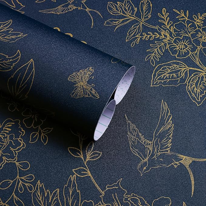 A close-up of a rolled sheet of dark blue wallpaper featuring intricate gold line drawings of flowers, leaves, a butterfly, and a bird. Perfect for adding elegance and detail to any dark and moody interior design.