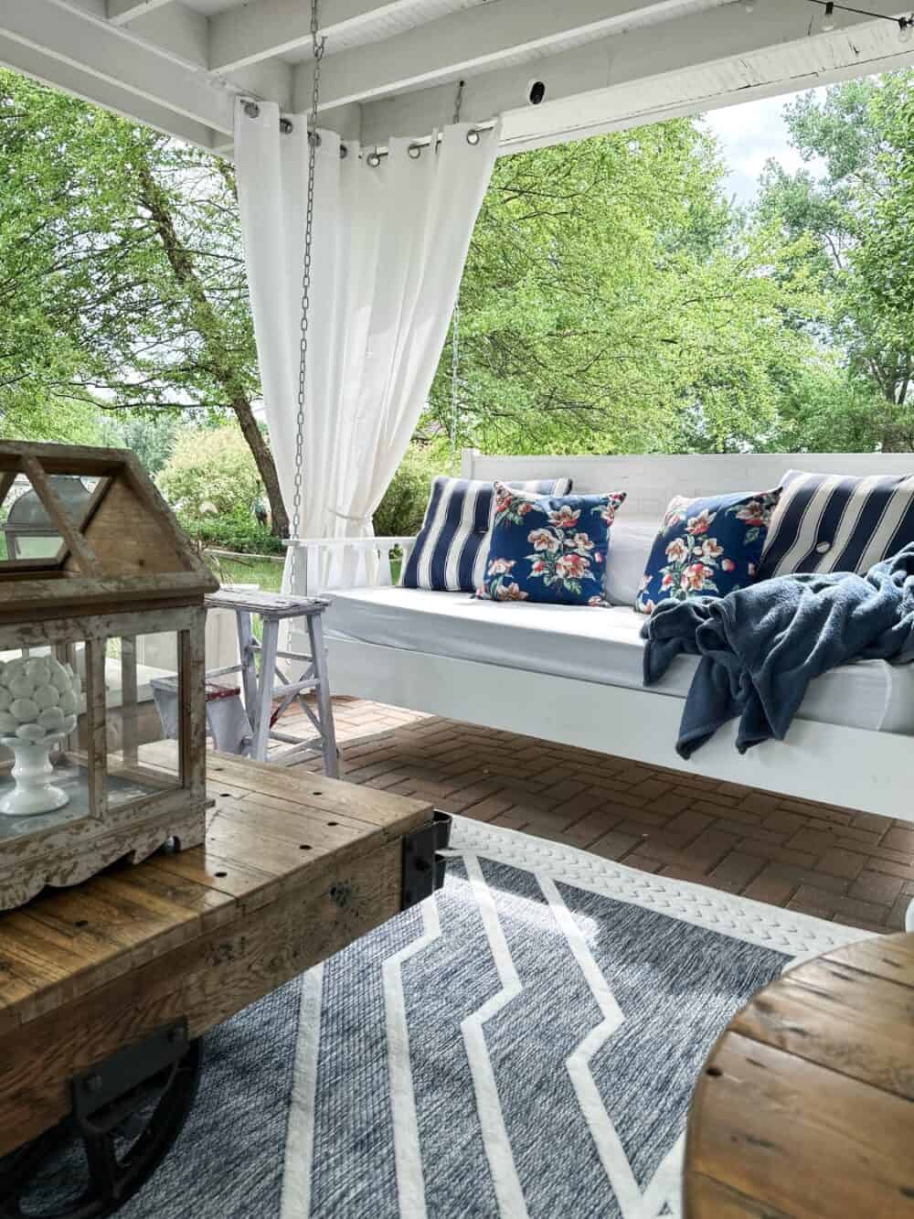 Photo of the swing bed in our outdoor living room with blue and white pillows and rug