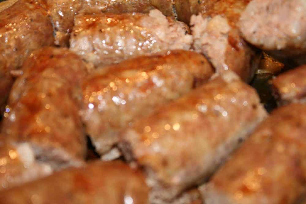 Close-up of several golden-brown sausages, showcasing their glistening, slightly crispy surfaces. The sausages are tightly packed, suggesting they have been freshly cooked or grilled.