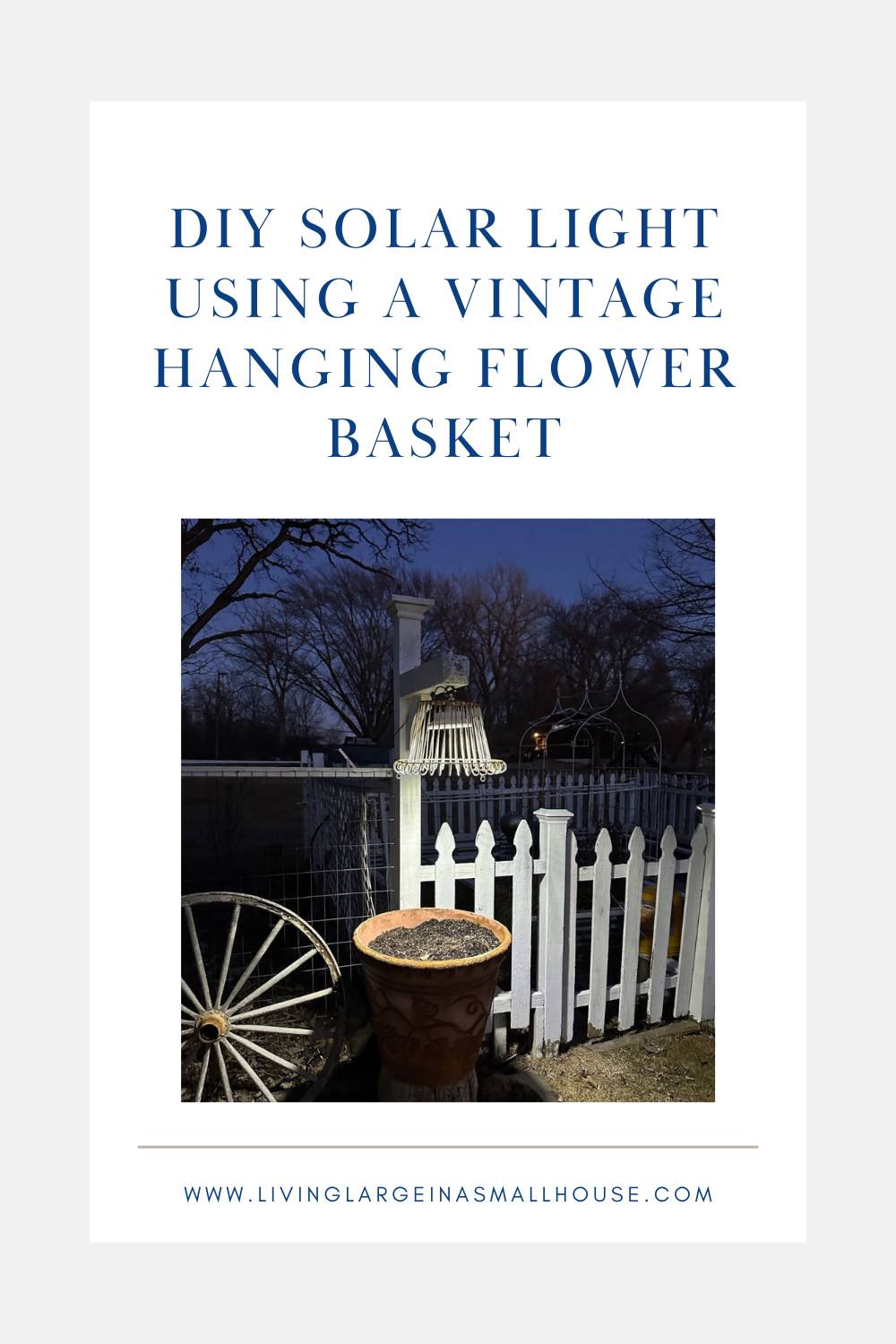 A solar light setup using a vintage hanging flower basket is shown by a white picket fence. The light illuminates the garden, casting a charming glow reminiscent of a wine bottle candle against bare trees in the background. Text reads "DIY solar light using a vintage hanging flower basket.