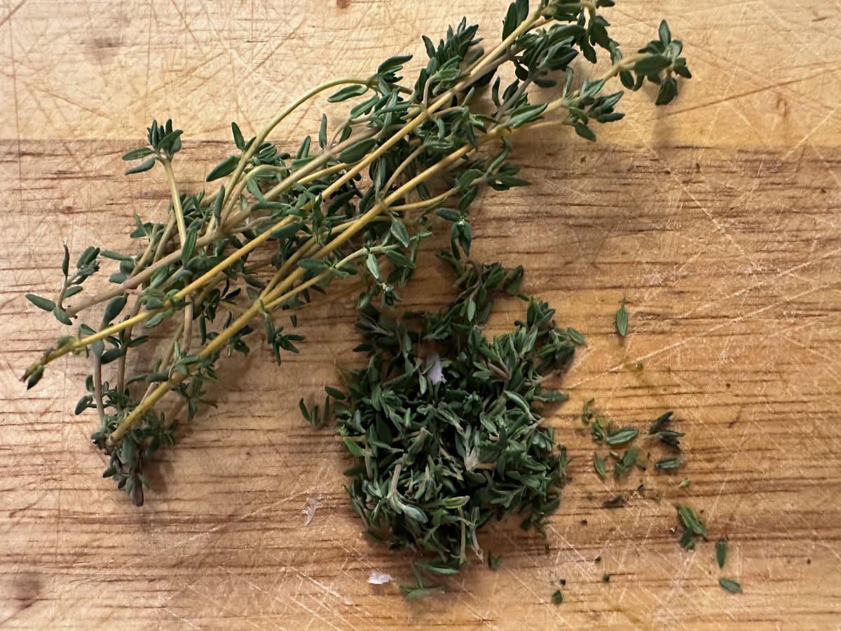 Fresh thyme sprigs and chopped thyme on a wooden cutting board.