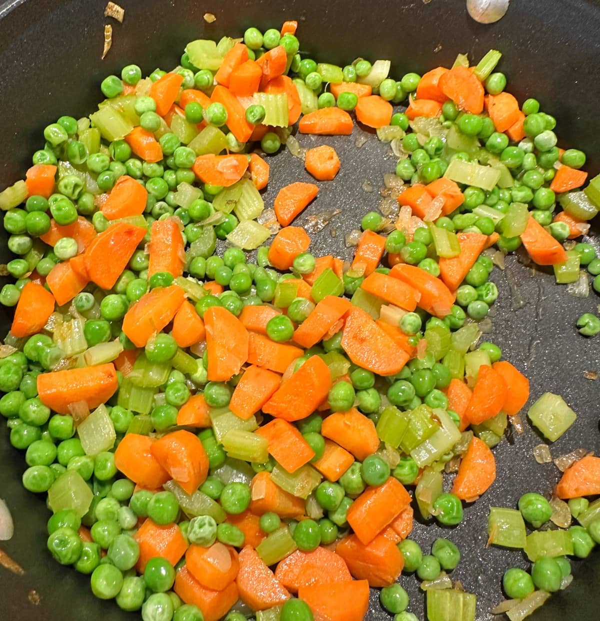 A skillet filled with sautéed mixed vegetables, including bright orange carrots, green peas, and celery, creating a colorful and healthy dish.