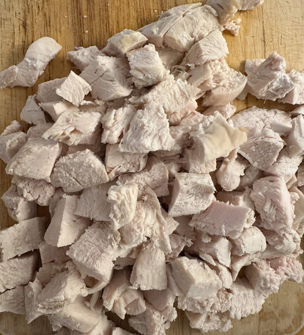 Diced cooked chicken pieces on a wooden cutting board.