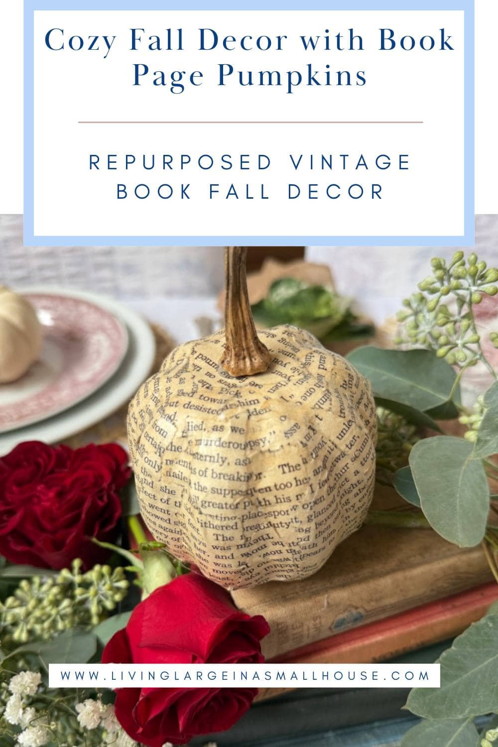 A book page pumpkin sits among red roses, greenery, stacked books, and elegant tableware, inspiring cozy fall decor ideas with a literary touch.