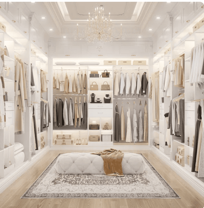 Luxurious walk-in closet perfect for downsizing to a smaller home, with organized clothes, handbags, and shoes on open shelves. White décor, chandelier, tufted bench with blanket, and elegant rug create a sophisticated atmosphere.