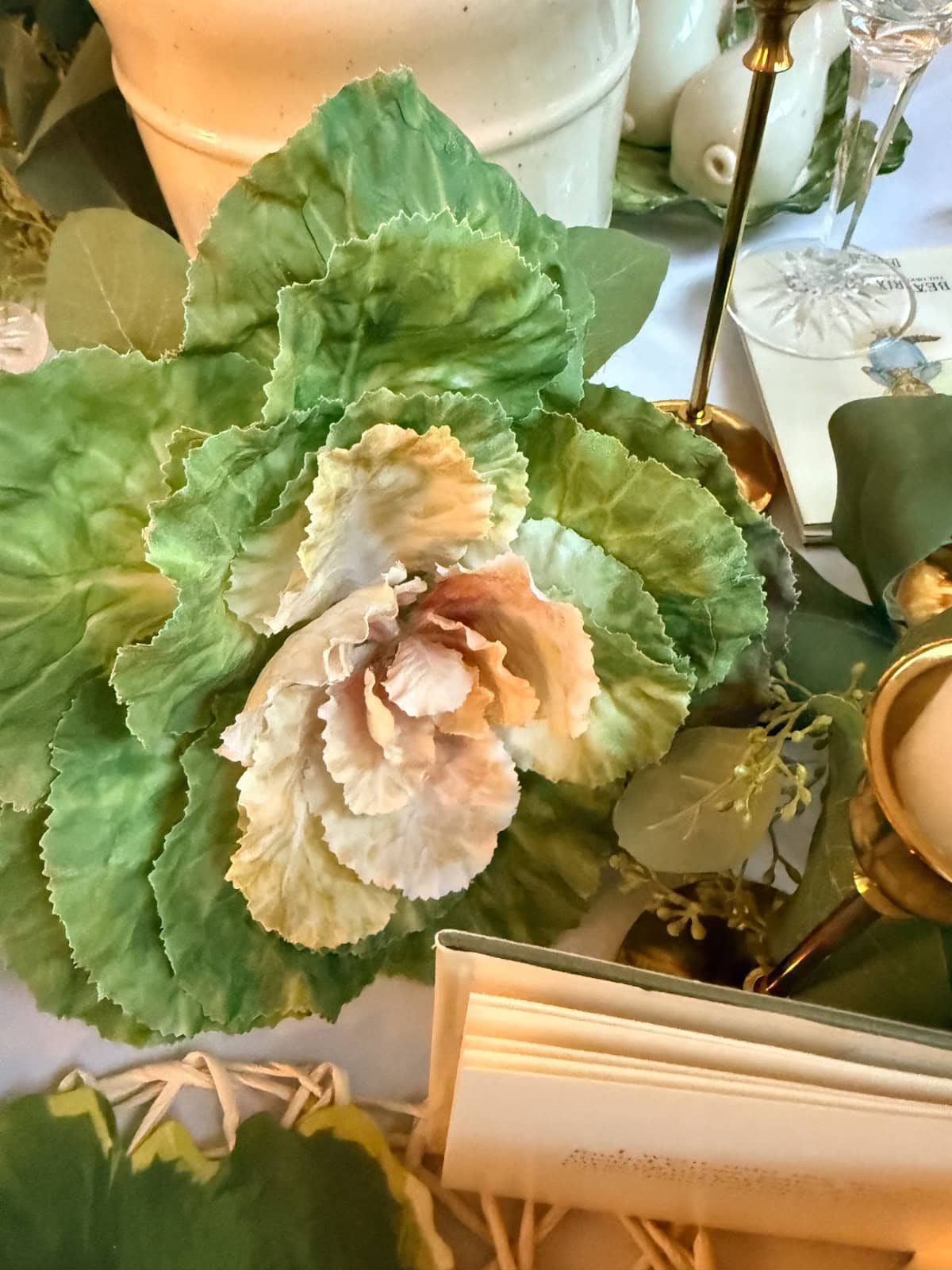 A close-up of a large, ruffled artificial green and white cabbage leaf centerpiece on a decorated table, perfect for a spring home tour, surrounded by candles, greenery, and elegant white dishes.