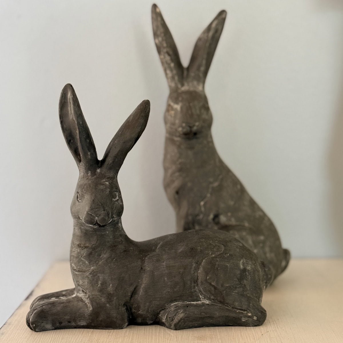 Two dark, textured ceramic rabbit sculptures are positioned on a light-colored surface—perfect for a Peter Rabbit Tablescape or Spring Home Tour. One rabbit reclines in the foreground, while the other sits upright in the background, both facing slightly right.