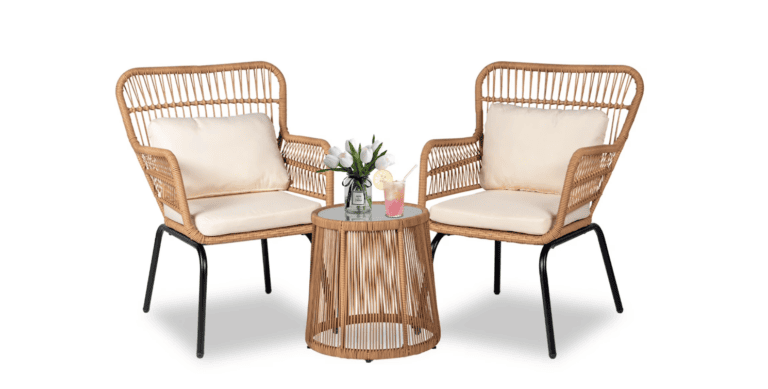 Two wicker armchairs with cream cushions are placed on either side of a round wicker side table with a glass top. Perfect for relaxing after a shopping trip, the table holds a small plant, a pink drink, and a yellow drink against a white background.