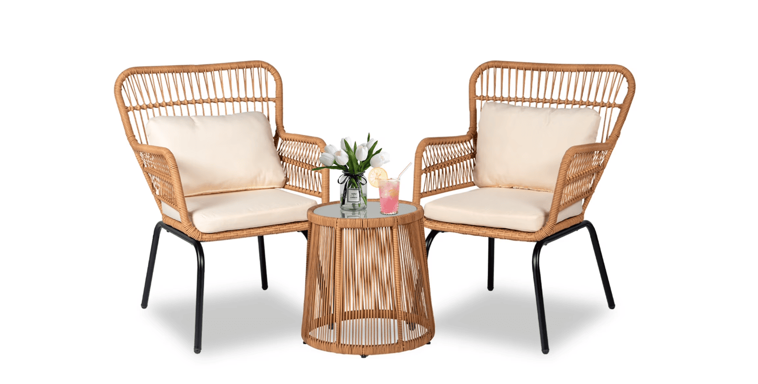 Two wicker armchairs with cream cushions are placed on either side of a round wicker side table with a glass top. Perfect for relaxing after a shopping trip, the table holds a small plant, a pink drink, and a yellow drink against a white background.