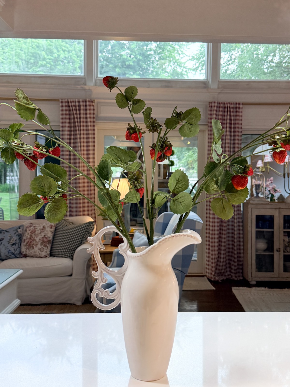 A white vase with green stems and red berries—a simple way to refresh your home for summer in a cozy, sunlit living room.