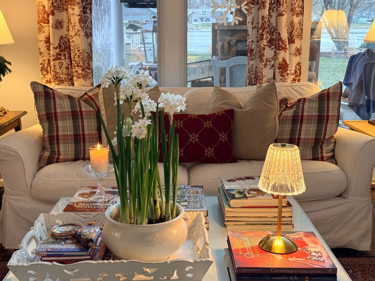 A cozy living room shows how to decorate a small home beautifully with plaid pillows, books, and a glowing lamp and candle.