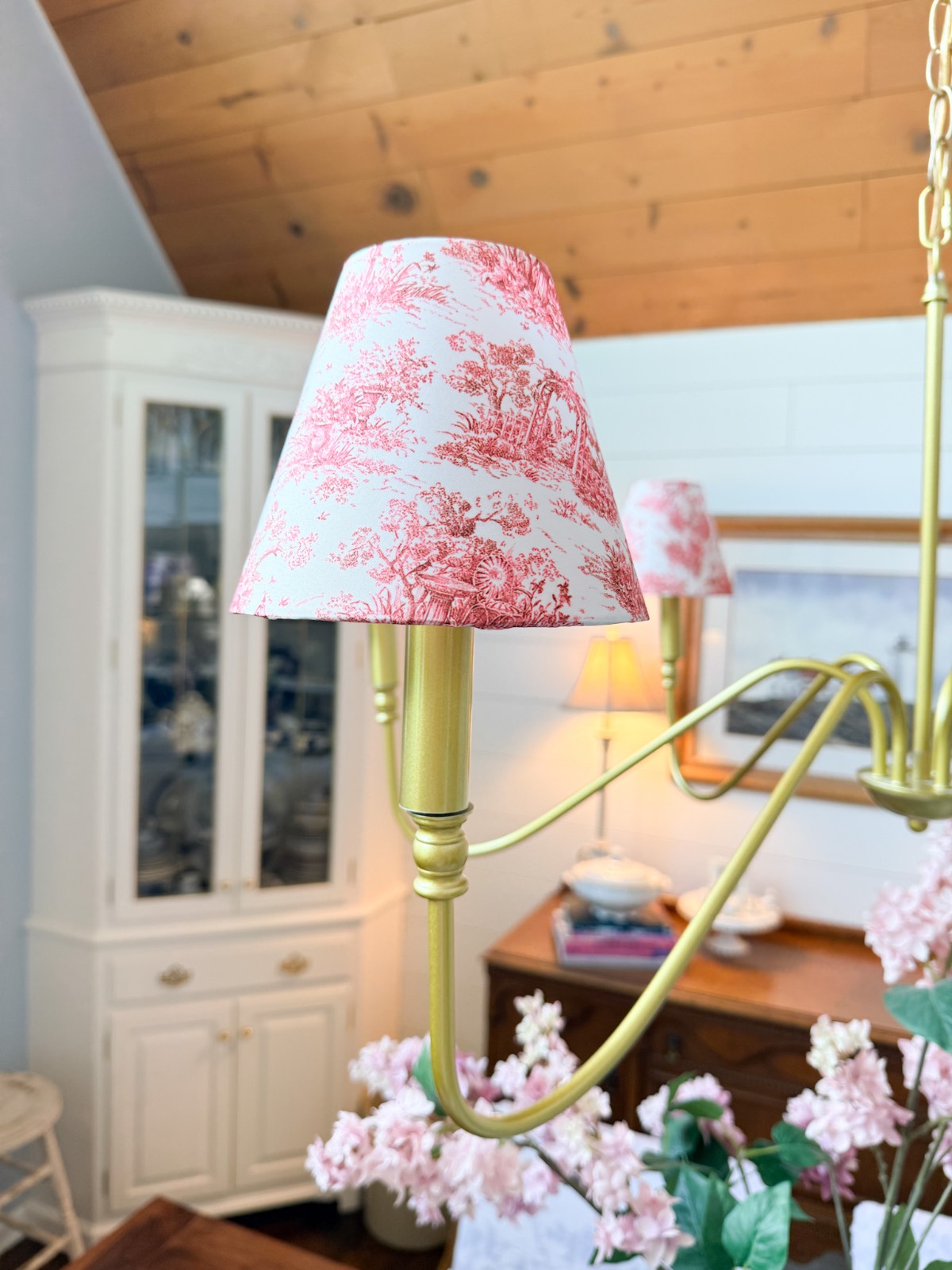Close-up of a gold chandelier with a pink and white lampshade—a chic way to refresh your home for summer.