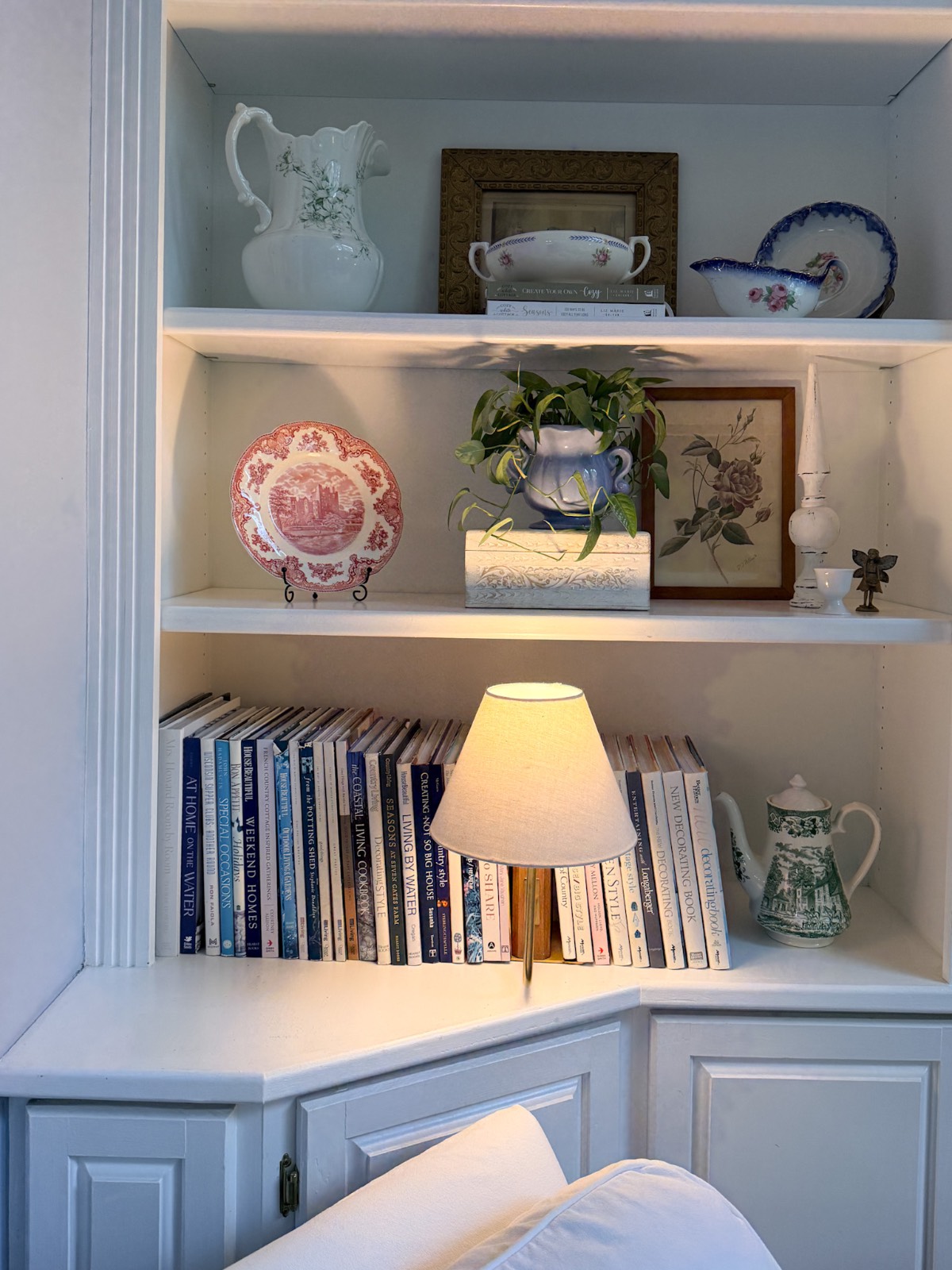 White built-in shelves styled for summer: books, a lit lamp, ceramics, art, plants—how to refresh your home for summer décor.