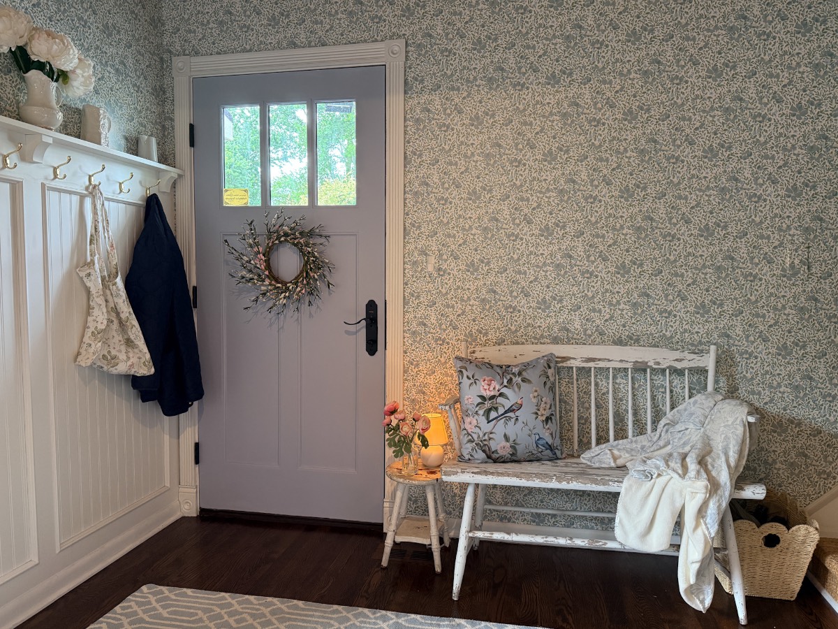 Cozy entryway with a lavender door, floral wreath, and bench—see how to refresh your home for summer with inviting touches.