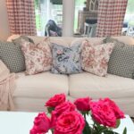 A white sofa with floral and plaid pillows shows how to refresh your home for summer with a striped blanket and pink roses.